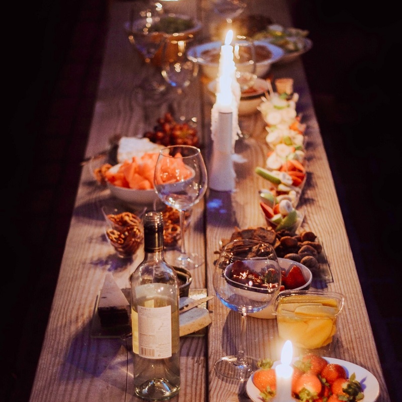 A long wooden table set with festive finger food without the fuss, candles, wine and wine glasses