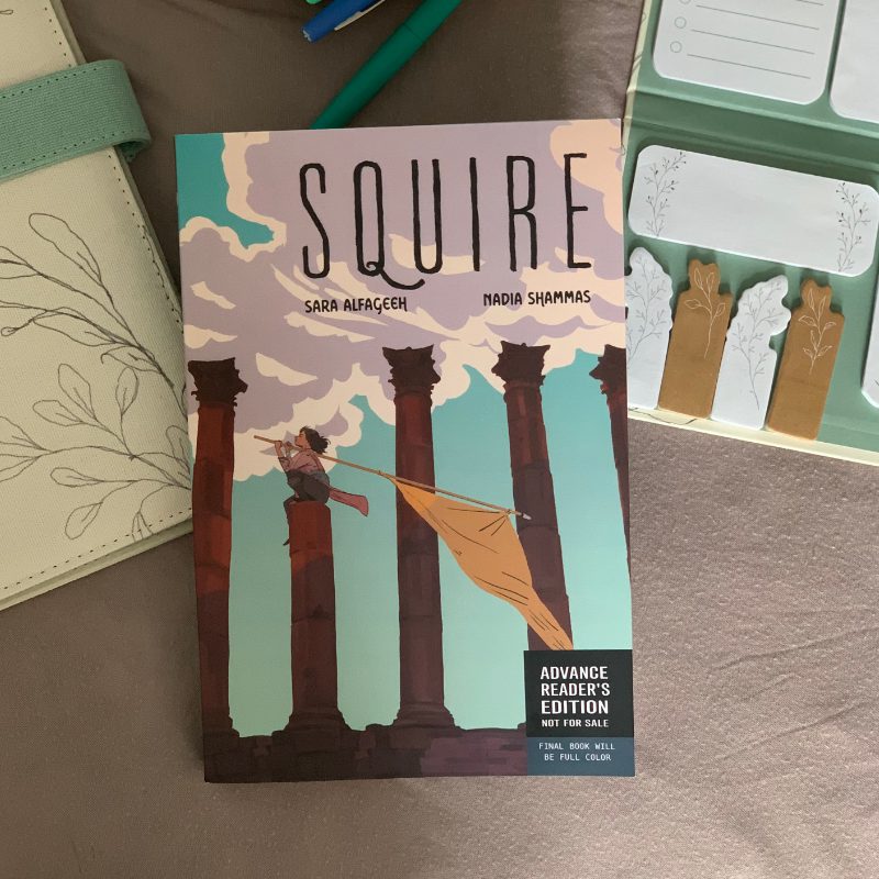 Flat lay of Squire in paperback surrounded by an open pencil case with pens sticking out, a note pad, and sticky notes pad.