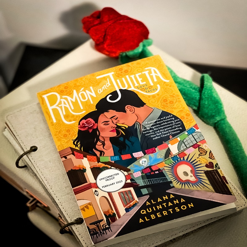 : A picture of Ramon and Julieta stacked on top of a book and record player with a fake rose next to the novel.