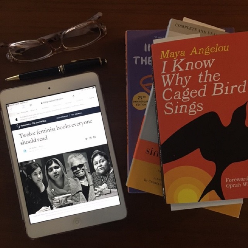 Photograph of iPad showing UN Women article next to some reading glasses, a pen and a selection of books including I Know Why the Caged Bird Sings by Maya Angelou