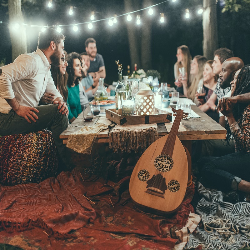 : How to Make the Most of Your Summer Coming to a Closing. A group of friends sitting outdoors under string lights around a small dinner table on the lawn.