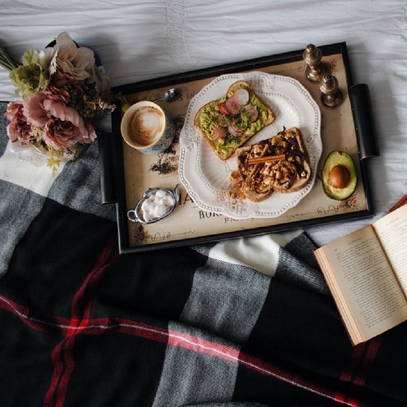Valentine’s Day Roundup: five hearty books about food and love. A breakfast tray of toast and an open book lying atop a bed and a red and black plaid blanket.