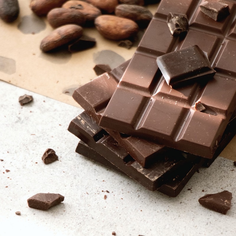 Photograph shows some milk and dark chocolate bars in the top right of the image with a number of cacao beans in the top left corner in honour of World Chocolate Day