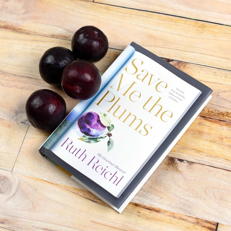 A copy of Save Me the Plums by Ruth Reichl sits next to plums