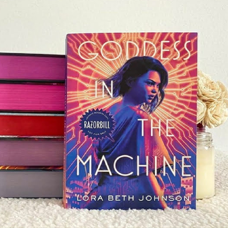 : A copy of Goddess in the Machine in front of a book stack.